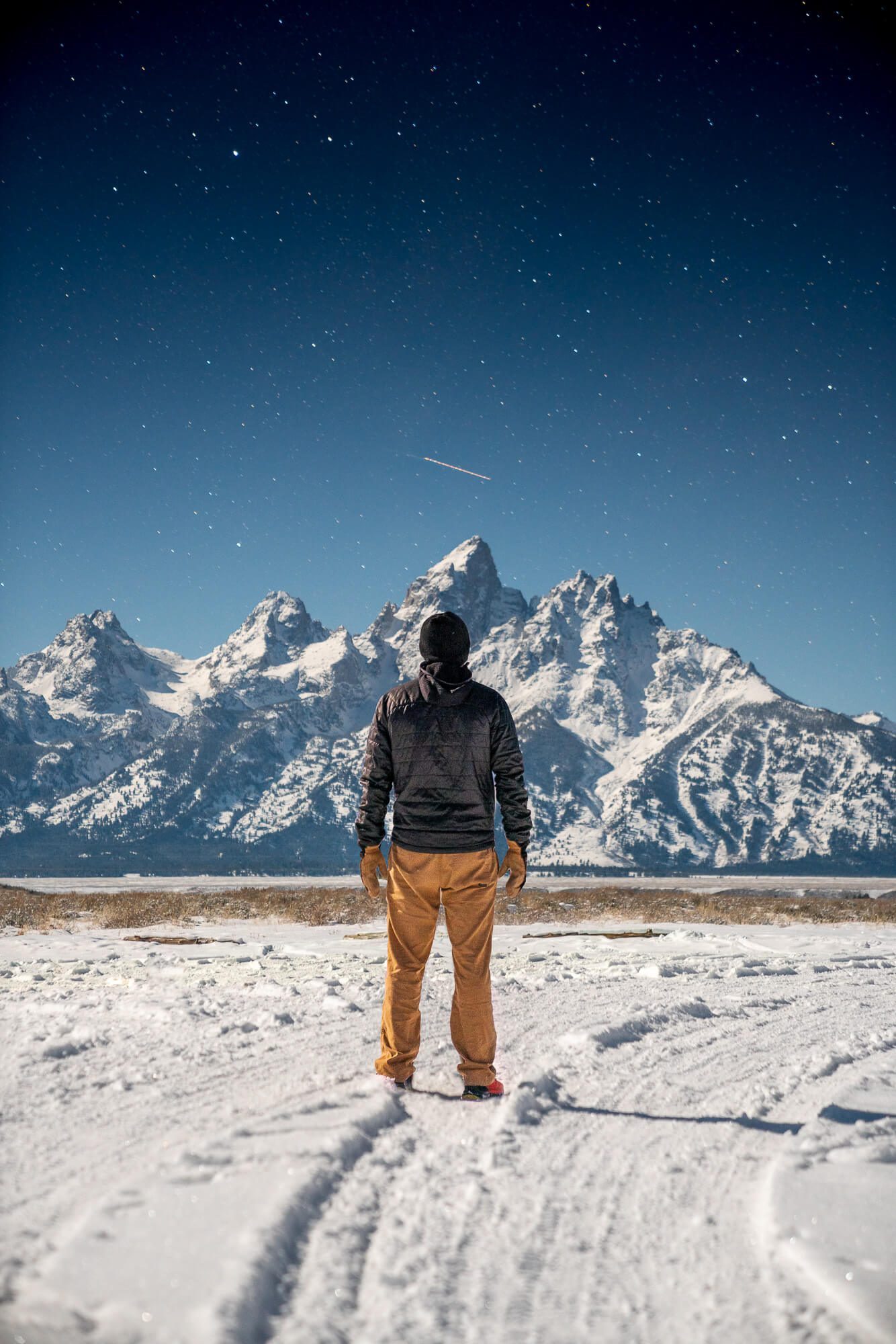 long exposure astro photo of man in a snowy field under a starry sky at grand teton national park | photo by jake landon schwartz