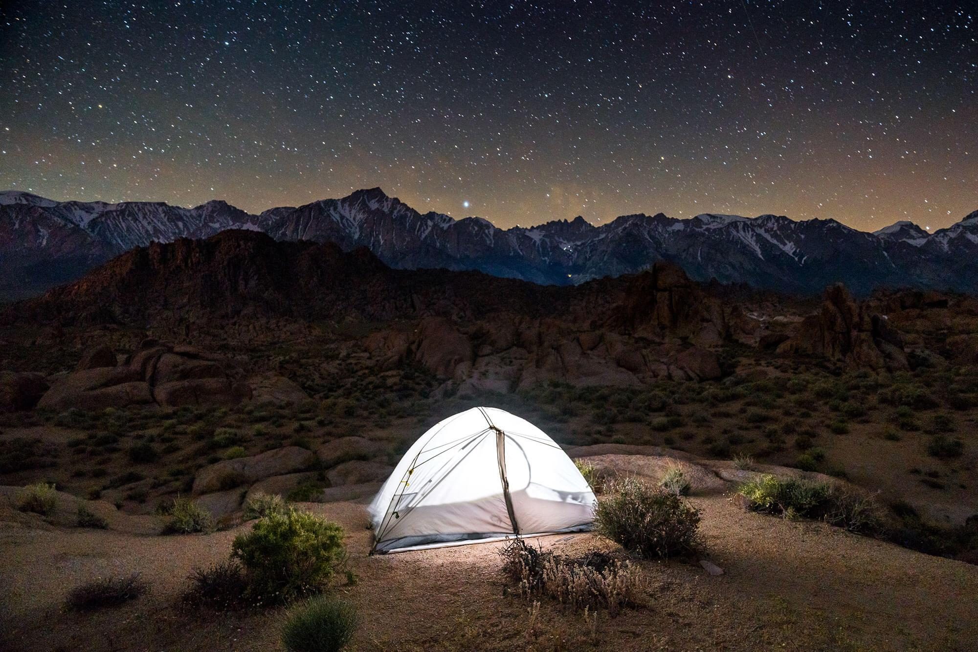 illuminated mountain hardwear tent in alabama hills california under a starry sky with mount whitney and the sierra nevada mountain range behind it | photo by jake landon schwartz